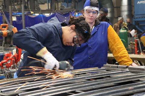 Two students working with powertools in a metal shop